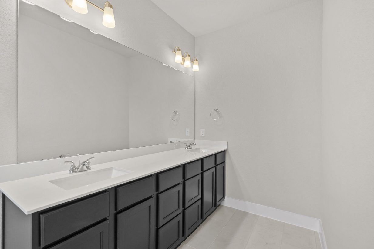 Image of a primary bathroom with a jack and jill countertop, black cabinets, and a large mirror