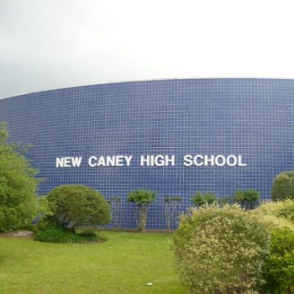School Students carrying backpacks and walking toward a modern New Caney ISD school building.
