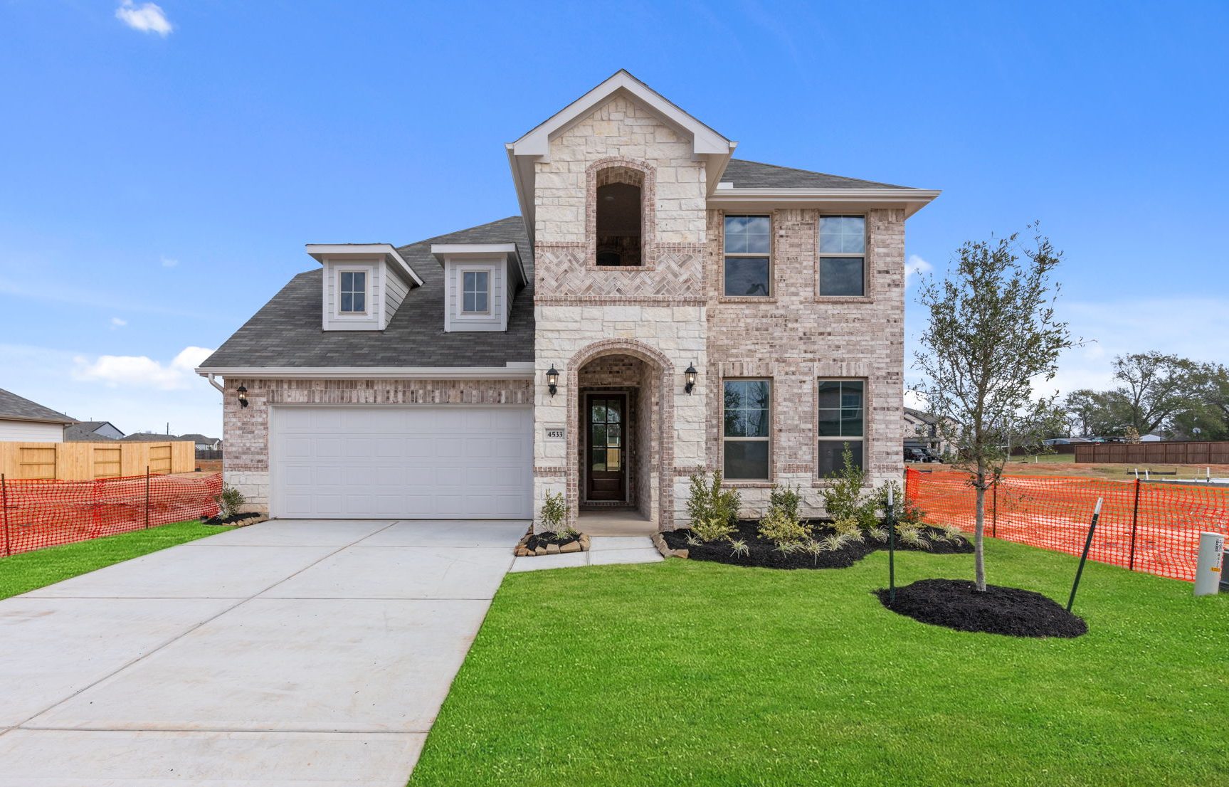 Image of a brick two story home with a white garage, cement driveway, green grass and a blue sky in the background