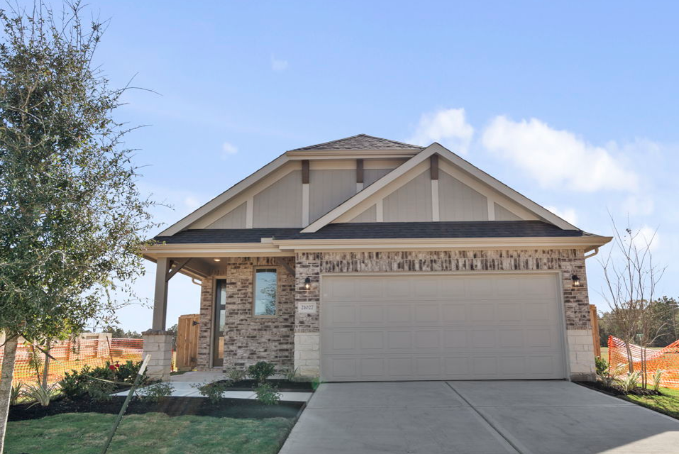 Image of a one story brick home with a tan garage door, cement driveway, a green grass front yard and a blue sky in the background