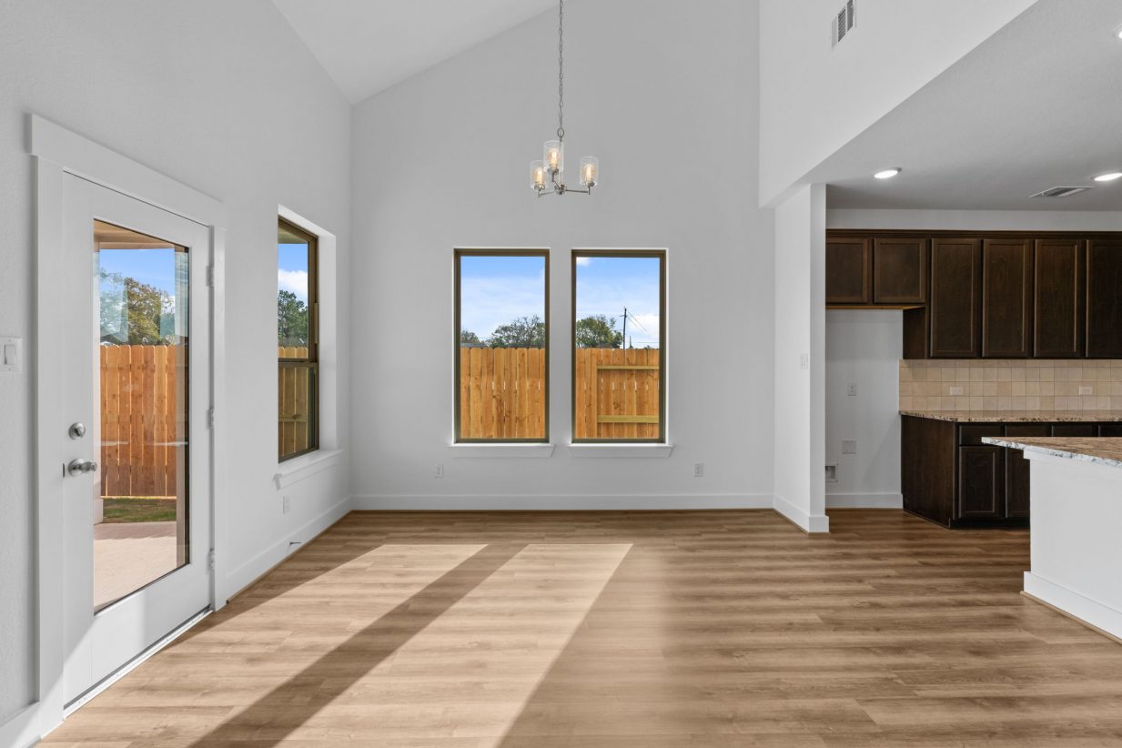 Image of a dining room with white walls, brown wood-look flooring, a back door with a window, and windows with brown trim