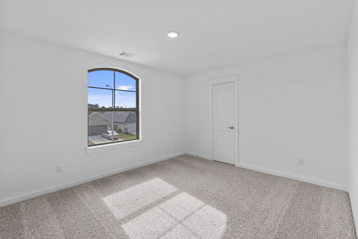 Image of a bedroom with tan carpeting, white walls and a window with brown trim