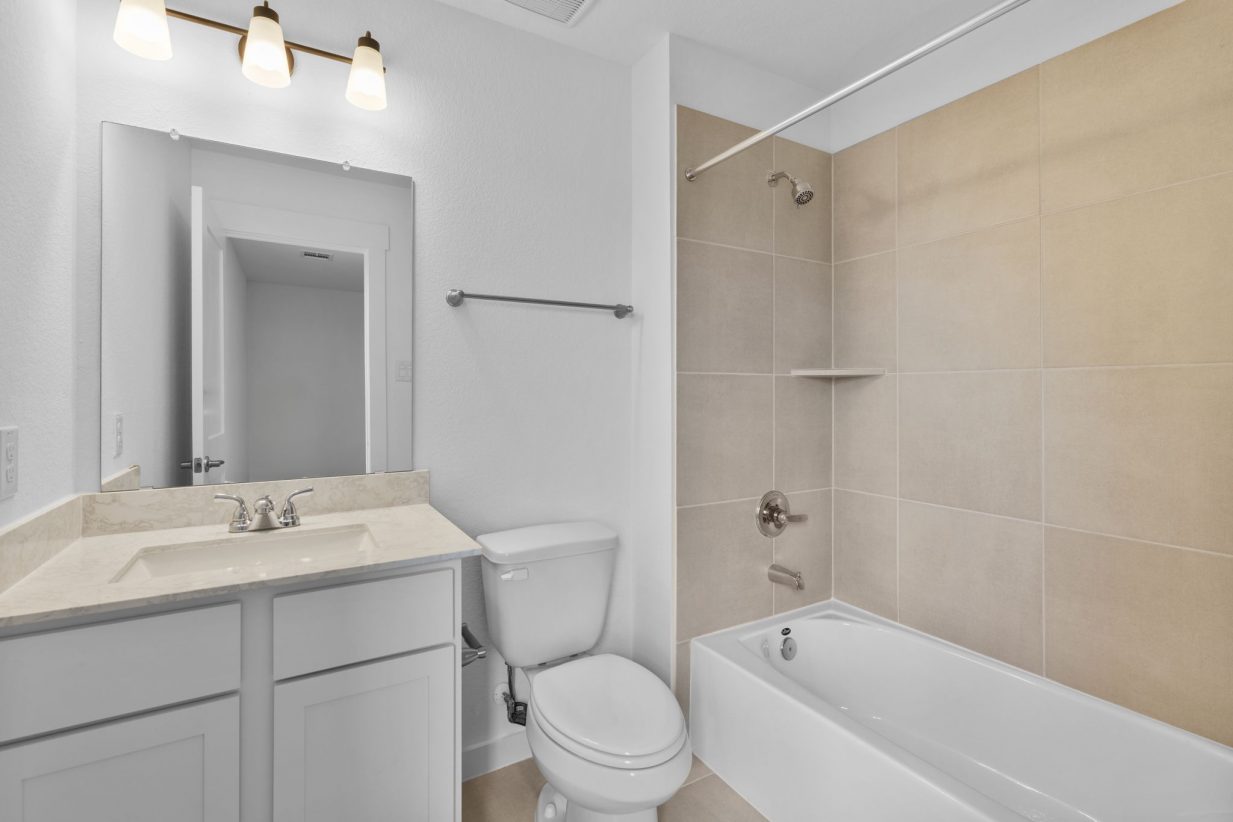 Image of a bathroom with a vanity, large mirror and a a shower with beige tiles and a white tub