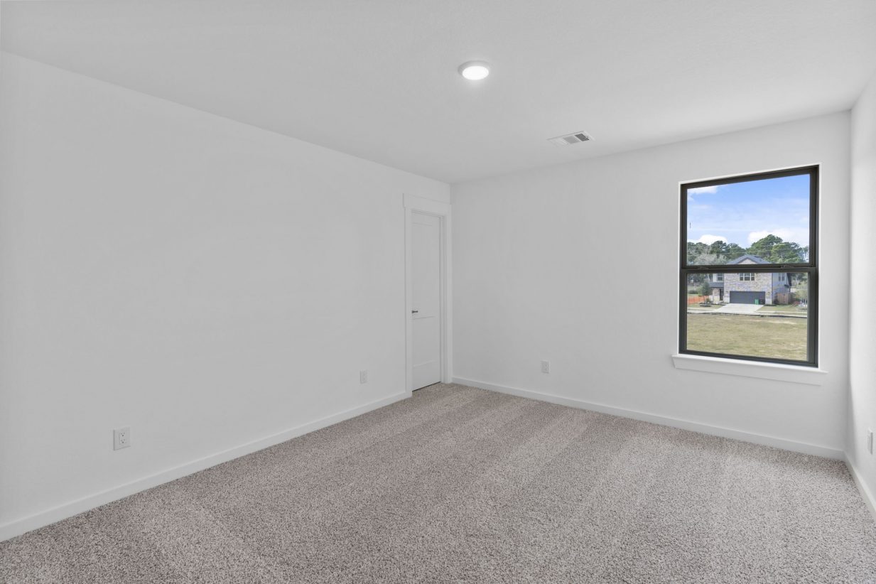 Image of a bedroom with tan carpeting, white walls and a window