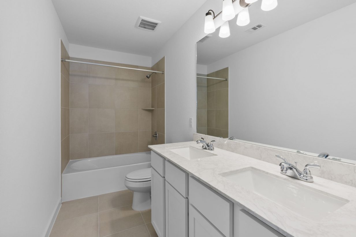 Image of a secondary bathroom with a jack and jill vanity, a large mirror, and a a shower and tub with tan tiles