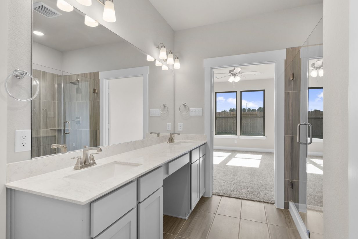 Image of a primary bath with a jack and jill vanity with light grey cabinets, white countertops, a large mirror and a standing shower