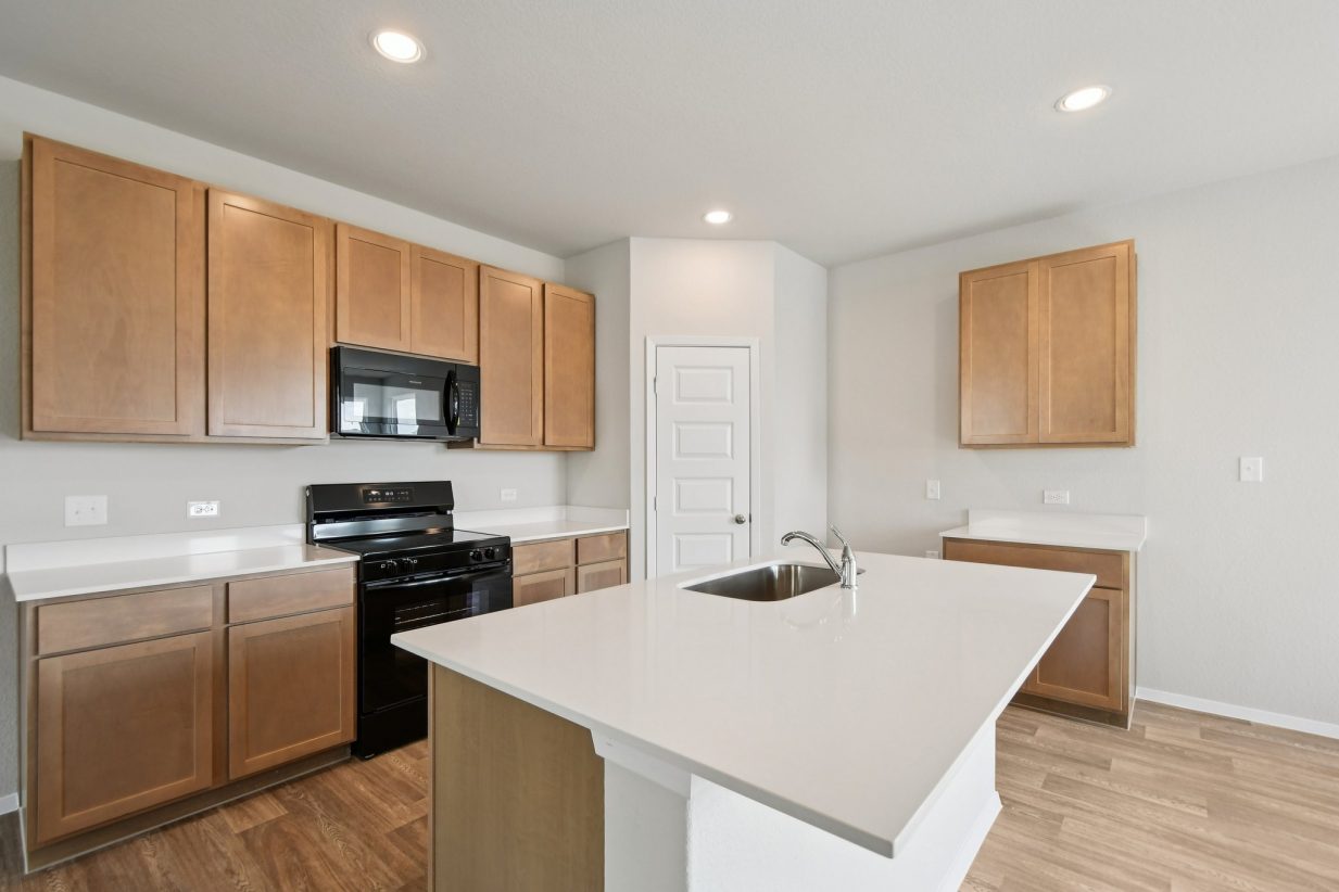 Image of a kitchen with light brown cabinets, a center island, white countertops and black appliances