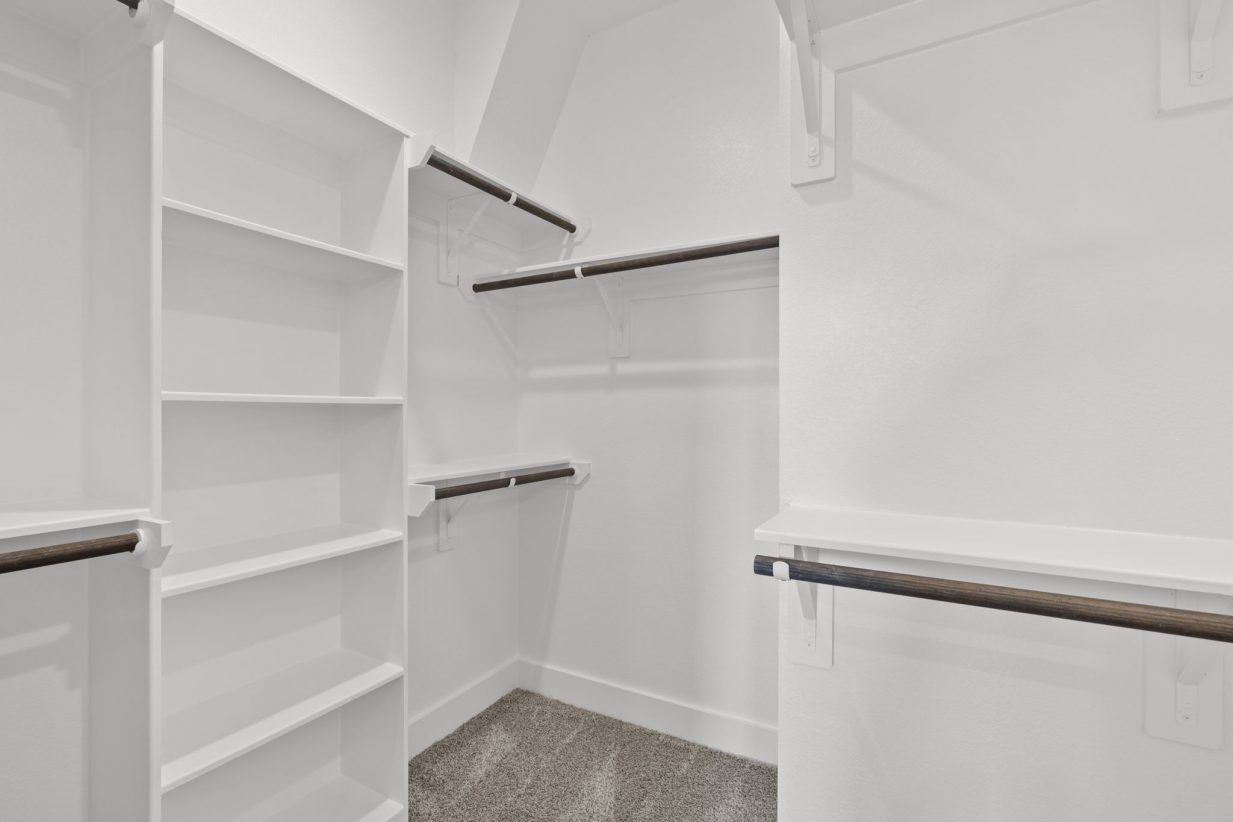 Image of a primary closet with white shelves and brown carpeting