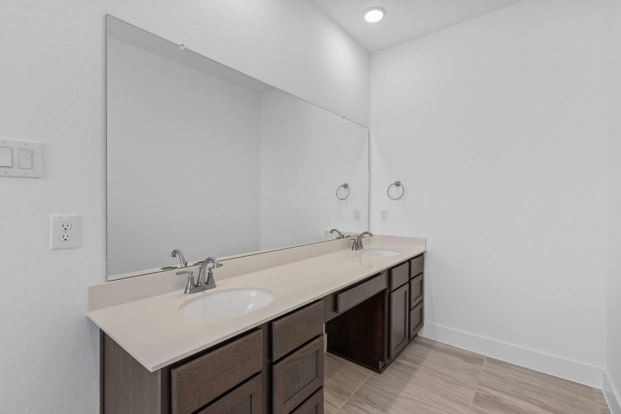 Image of a primary bathroom dual vanity with a large mirror and brown cabinets