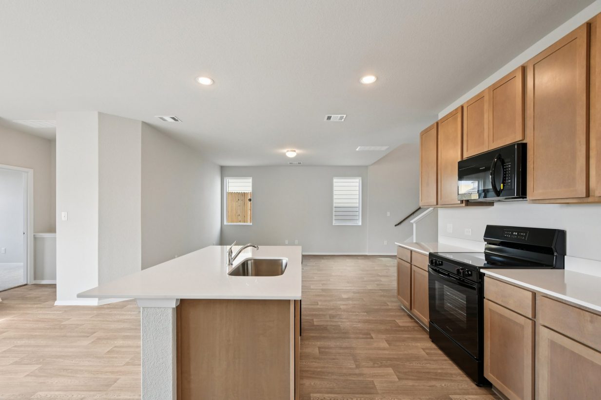 Image of a kitchen with light brown cabinets, white countertops, black appliances and a center island