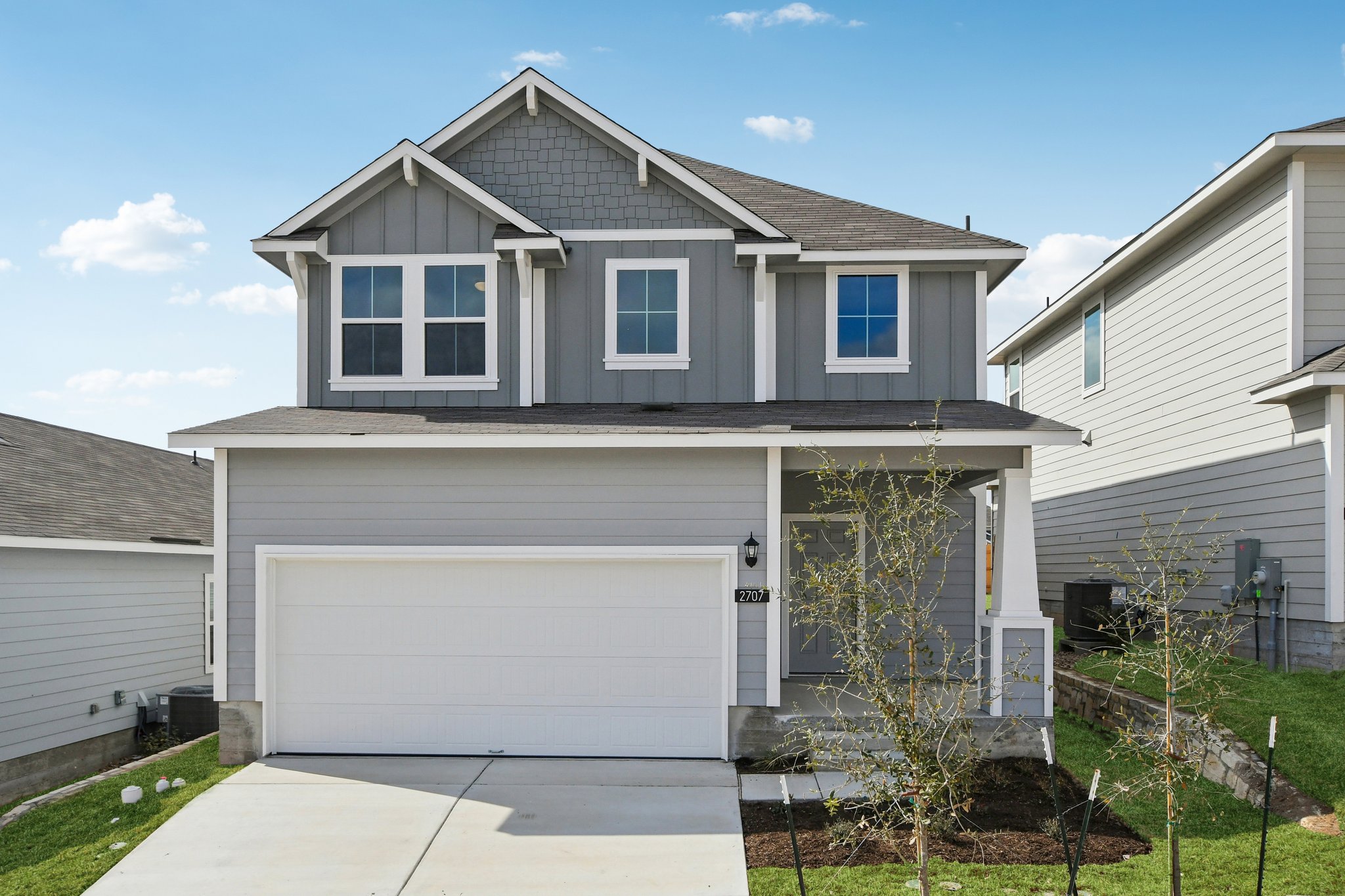 Image of a grey two story house front exterior with a white garage, a green grass front yard, and a blue sky in the background