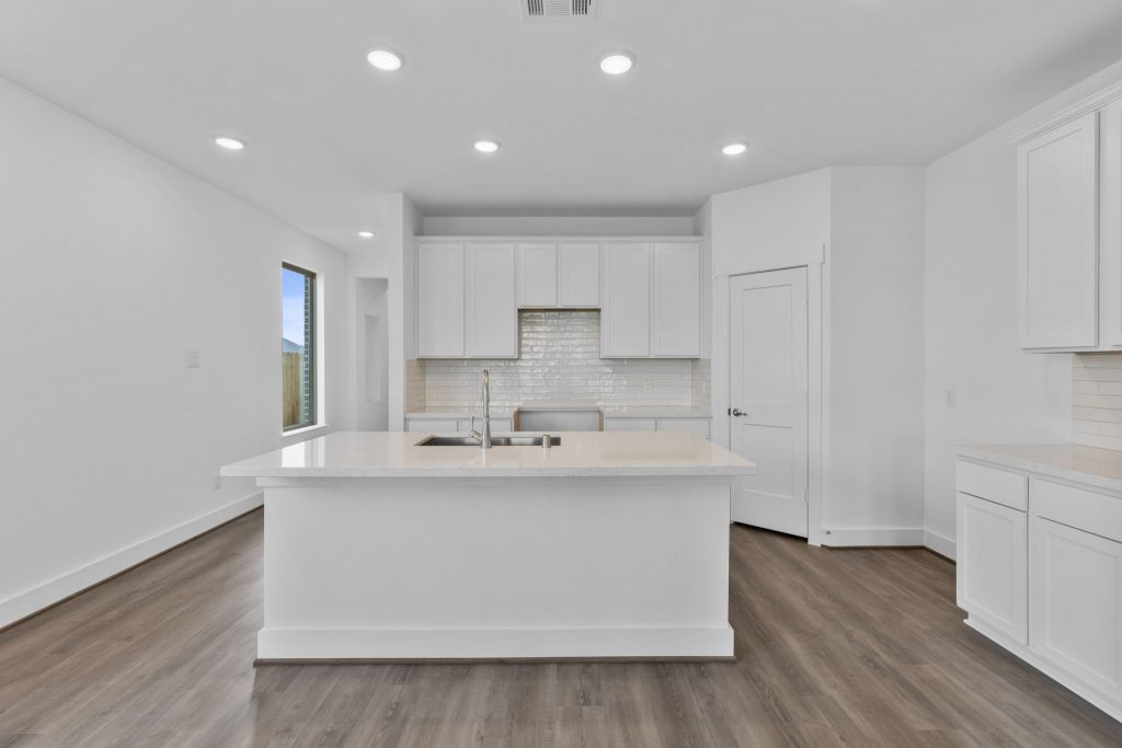 Image of a kitchen with a large center island, white cabinets, a corner pantry and light brown wood-look flooring