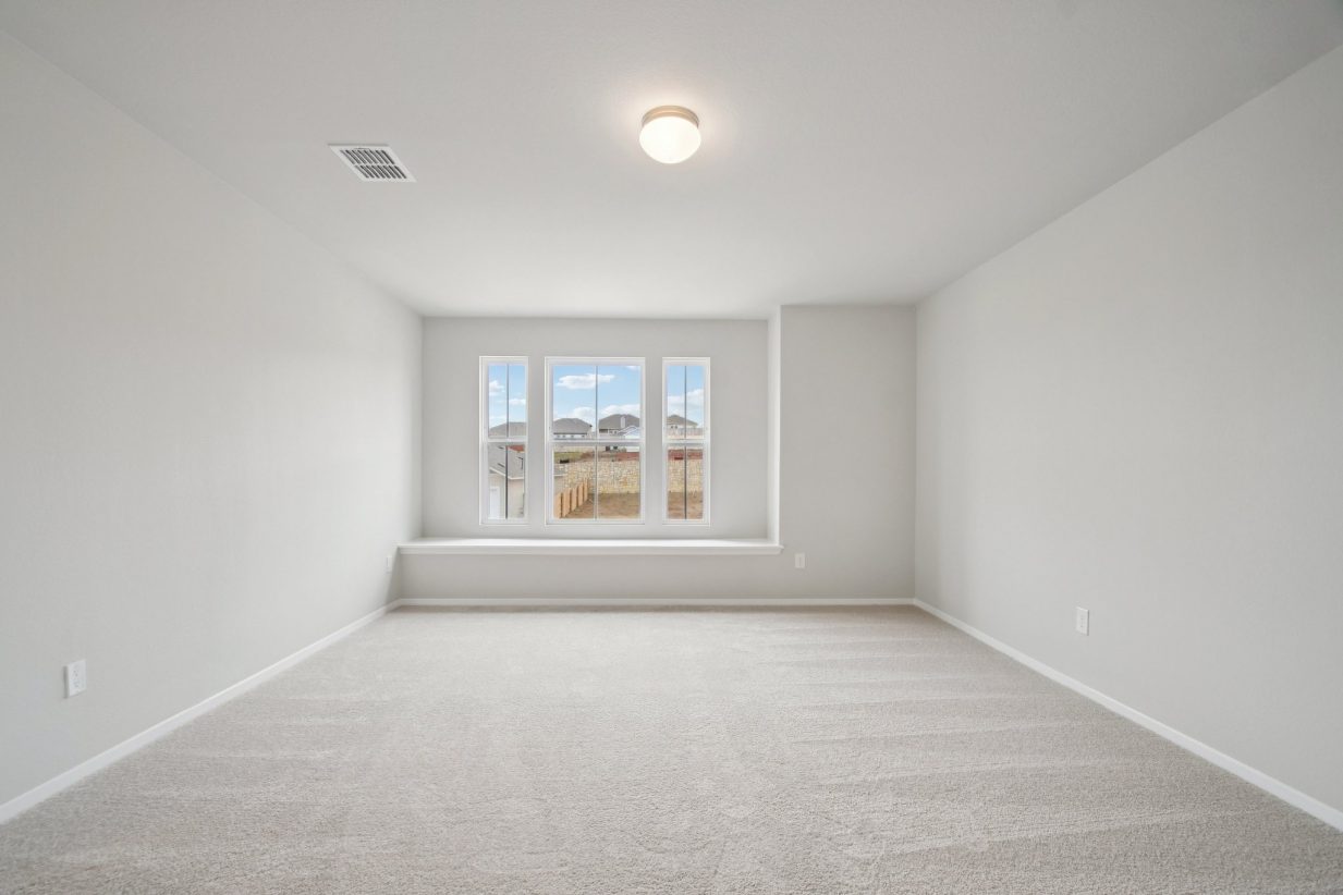 Image of a primary bedroom with light grey walls, tan carpeting, and a window with a ledge