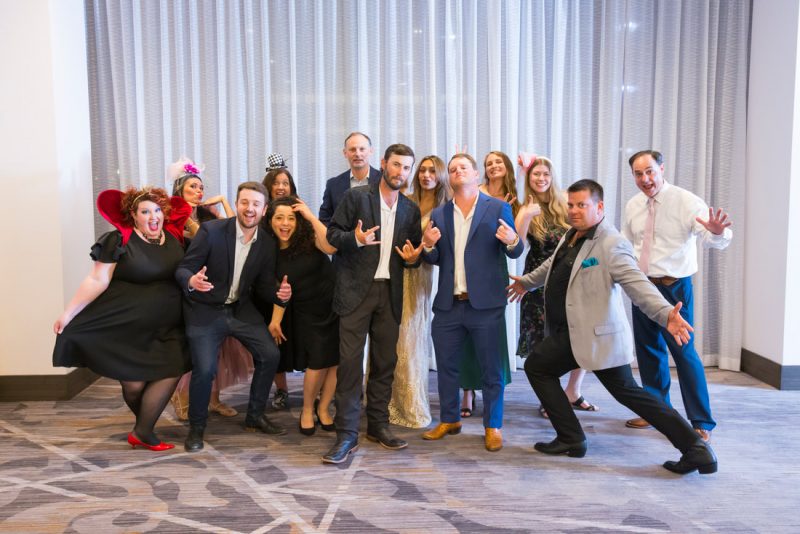 A group of people dressed up making funny faces and gestures in front of a white curtain and standing on carpet.