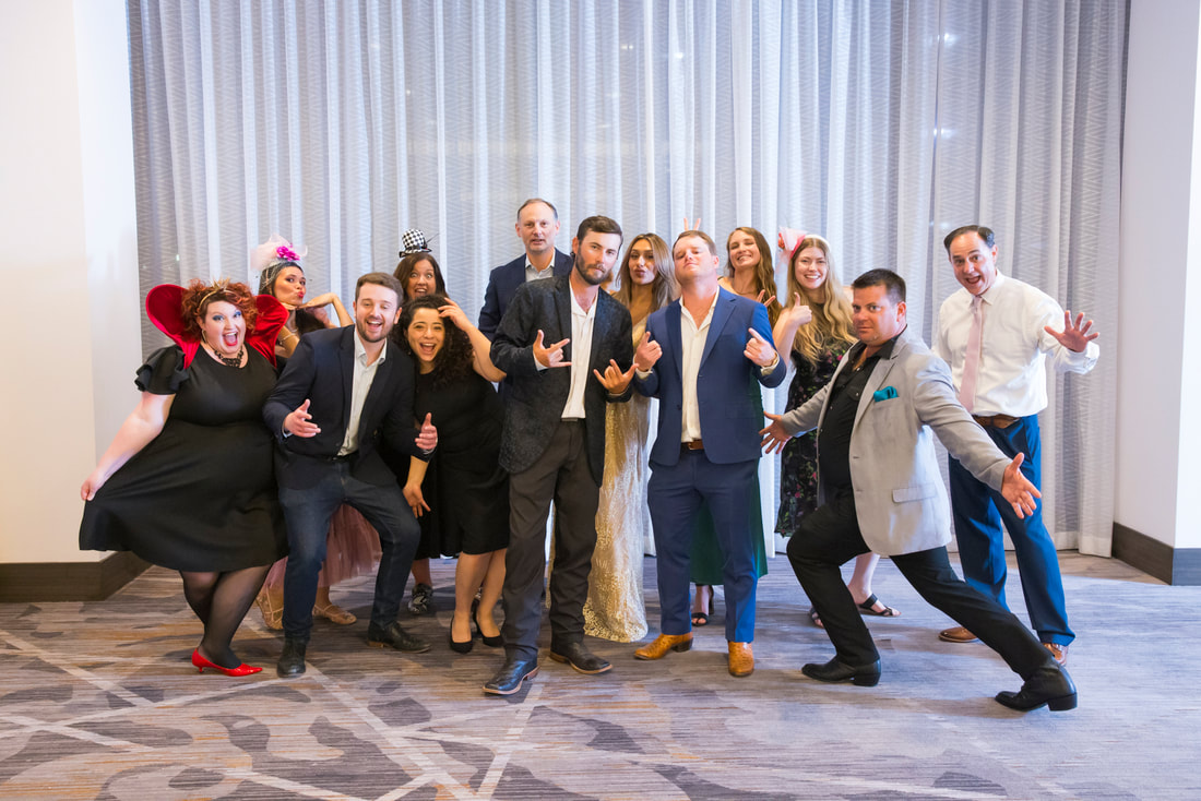 A group of people dressed up making funny faces and gestures in front of a white curtain and standing on carpet.
