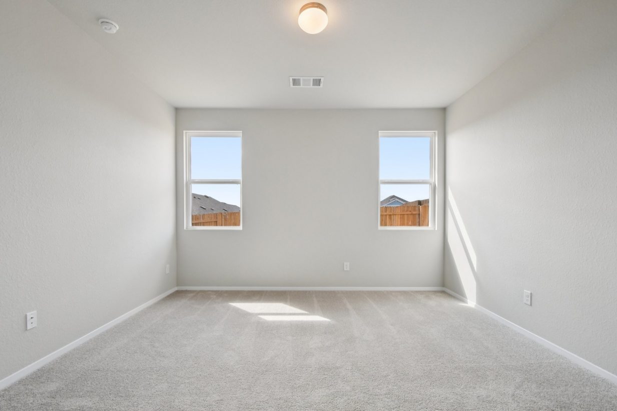 Image of a primary bedroom with light grey walls, tan carpeting, windows and white trim
