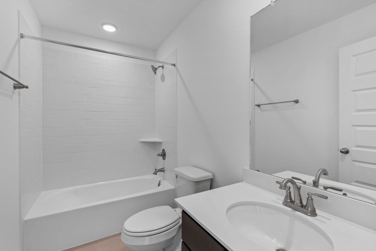 Image of a bedroom with white walls, a white vanity, a large mirror, white tile and a tub