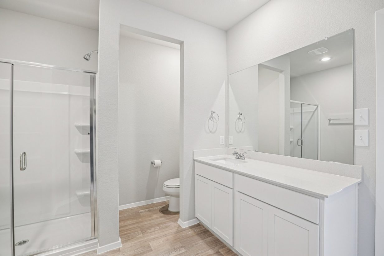 Image of a primary bathroom with a double vanity, white cabinets, a mirror and a walk-in shower