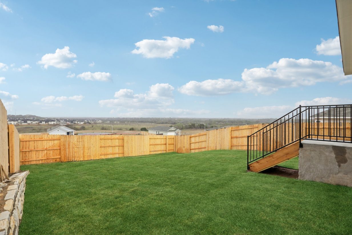 Image of a backyard with green grass, a wooden fence and a blue sky in the background