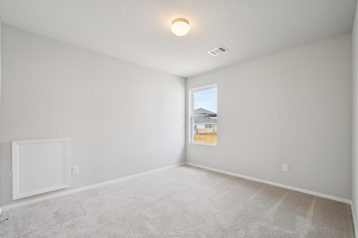Image of a bedroom with light grey walls, tan carpeting, and a window
