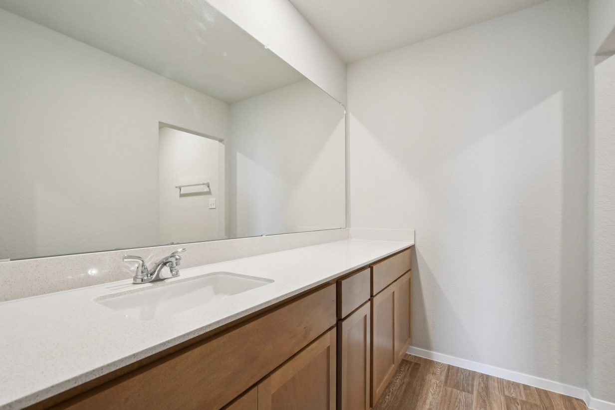 Image of a bathroom with brown cabinets, a white dual vanity, and a large vanity
