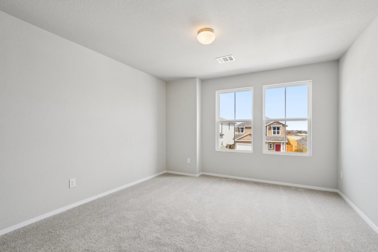 Image of a bedroom with light grey walls, tan carpeting, windows and white trim