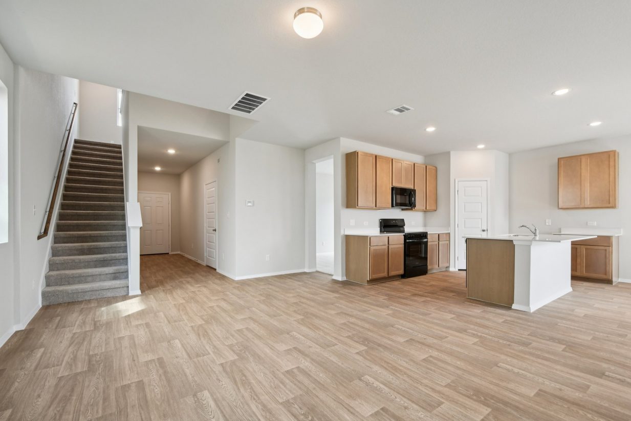 Image of a living room are with light brown vinyl flooring, a staircase, and a kitchen