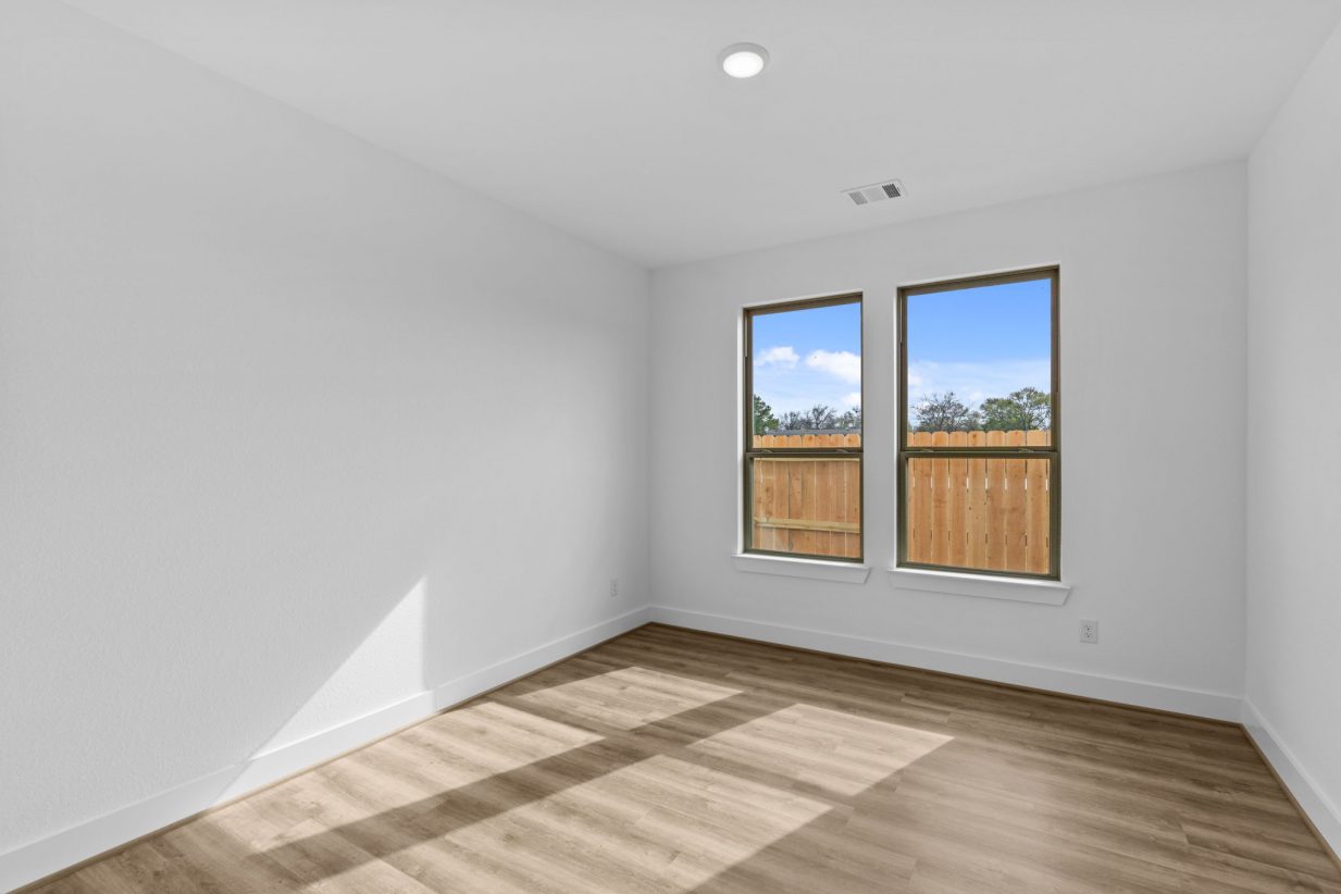 Image of a bedroom with brown wood-look flooring, white walls, and windows with brown trim