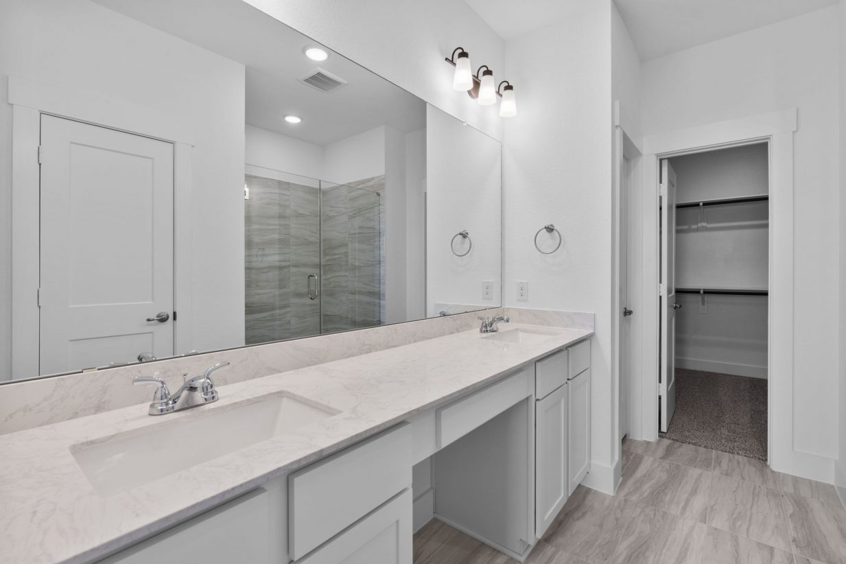 Image of a primary bath with a jack and jill vanity, a large mirror and grey cabinets