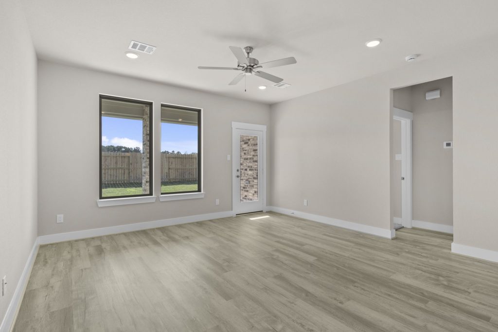 Image of a living room with beige walls, two windows, light brown flooring, and a ceiling fan