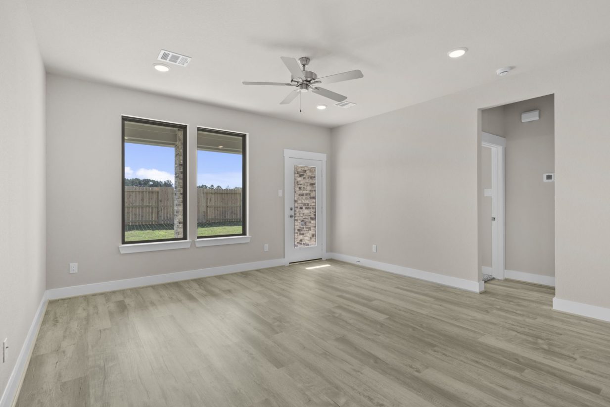 Image of a living room with beige walls, two windows, light brown flooring, and a ceiling fan