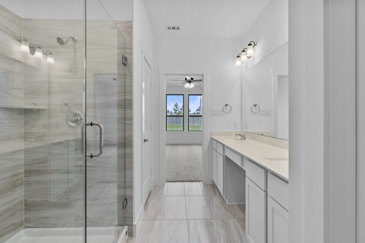 Image of a primary bathroom with a standing walk-in shower with glass doors, a jack and jill vanity and a large mirror