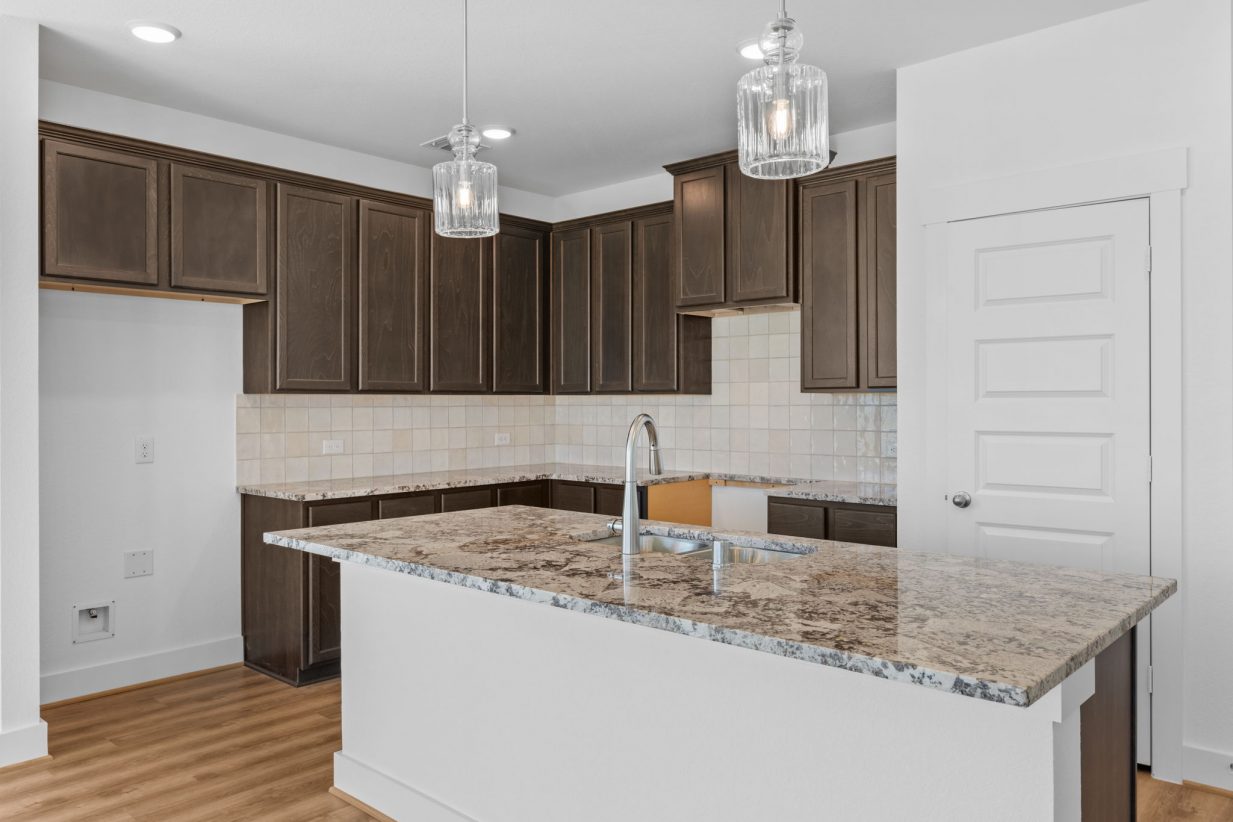 Image of a kitchen with brown cabinets, a large center island with granite countertops, and a pantry