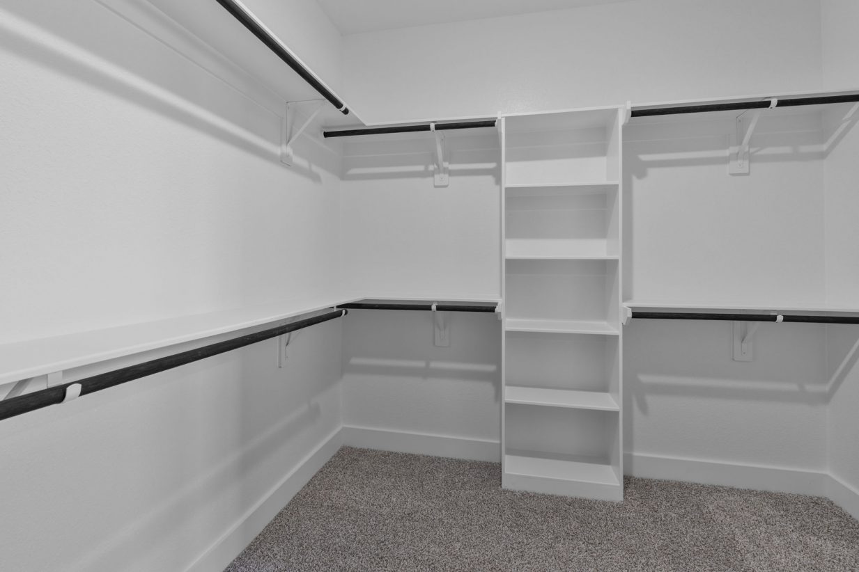 Image of a primary closet with white shelves and tan carpeting