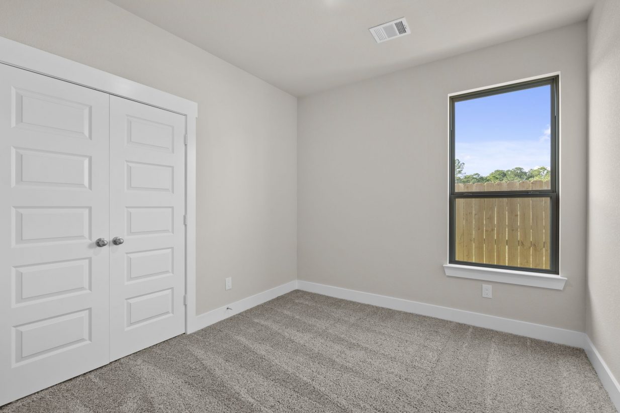 Image of a secondary bedroom with beige walls, tan carpeting, a window and a white door