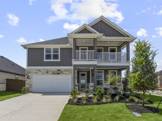 A two-story gray home, a white garage door, with white balcony fencing, concrete driveway, and a blue sky with clouds in the background.