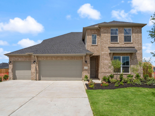 An image of two-story house with tan brick exterior, light brown double garages, green grass lawn, concrete drivewayd, and a blue sky background.