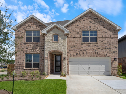 An image of a two story house, a white garage door, green grass lawn, concrete driveway with a blue sky background.