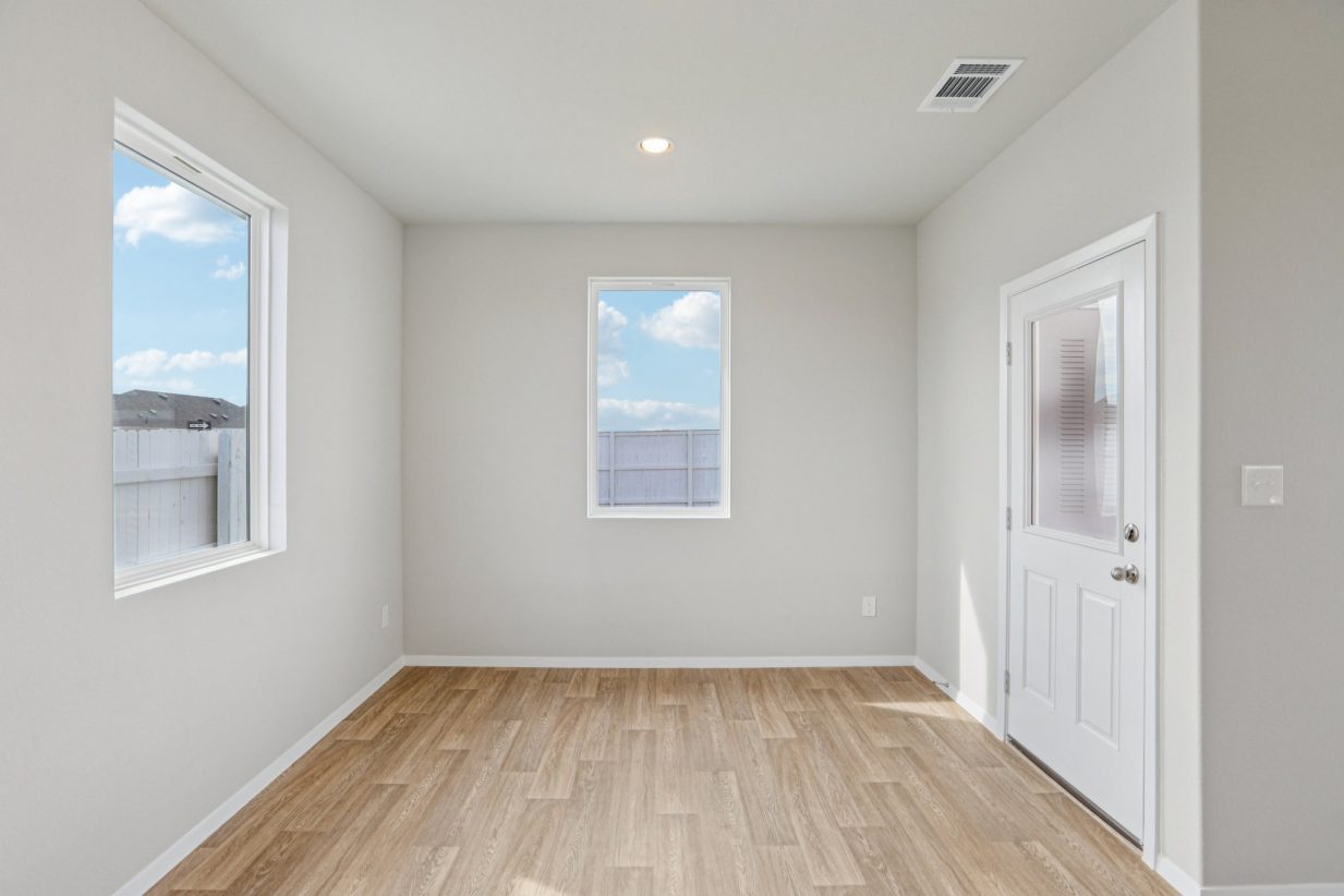 Image of a dining room with ligth grey walls, light brown wood-look flooring, a window and white trim
