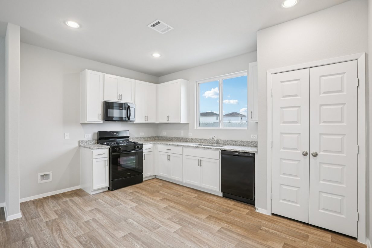 Image of an L-shaped kitchen with white cabinets, black appliances and a window above the sink
