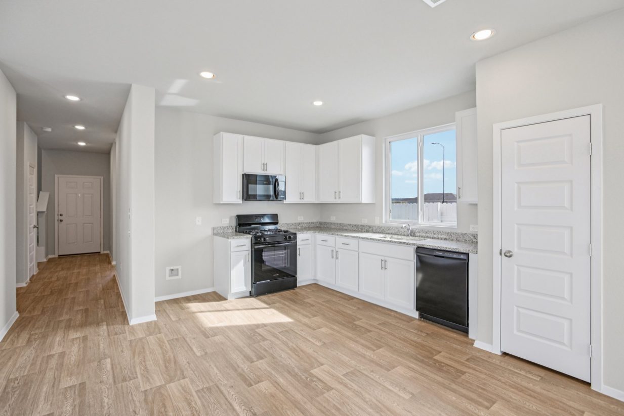 Image of a L-shaped kitchen with white cabinets, granite countertops, black appliances and a window above the sink