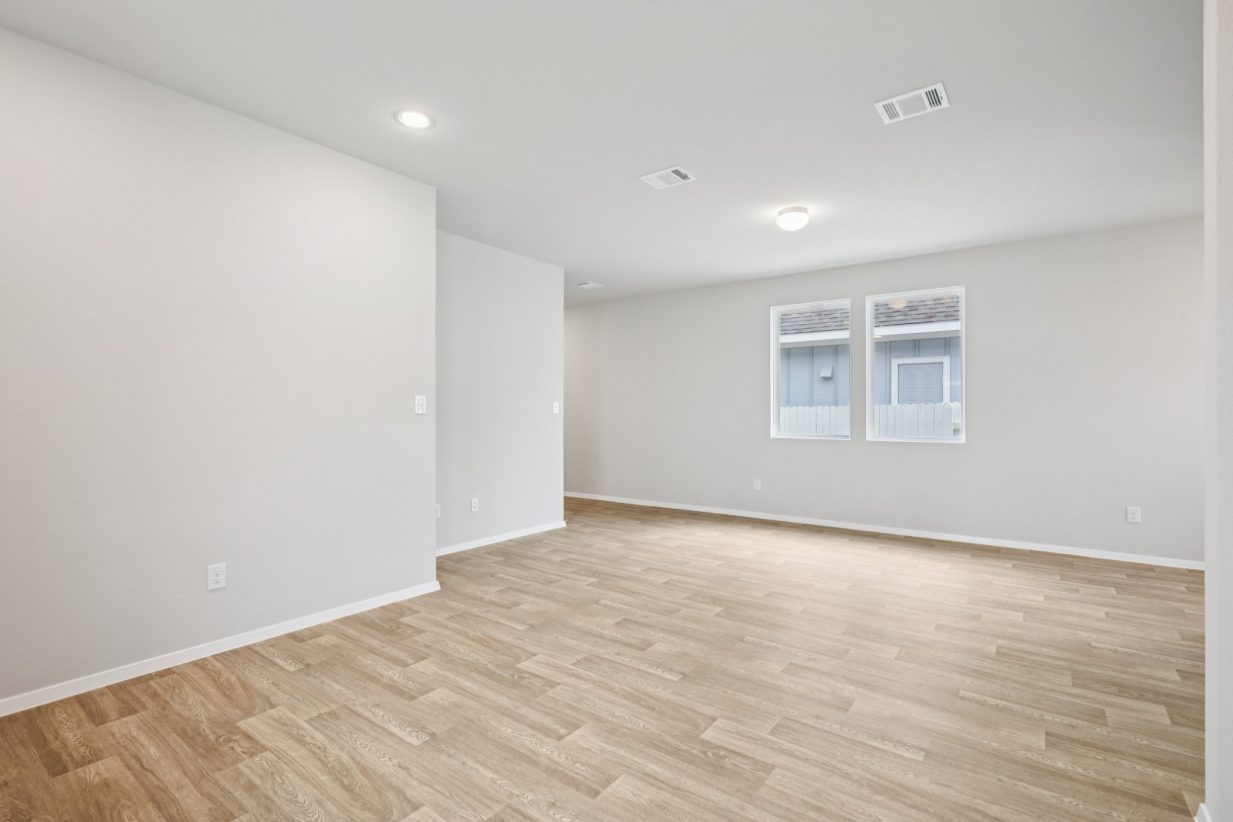 Image of a living and dining area with light grey walls, brown vinyl flooring and windows with white trim