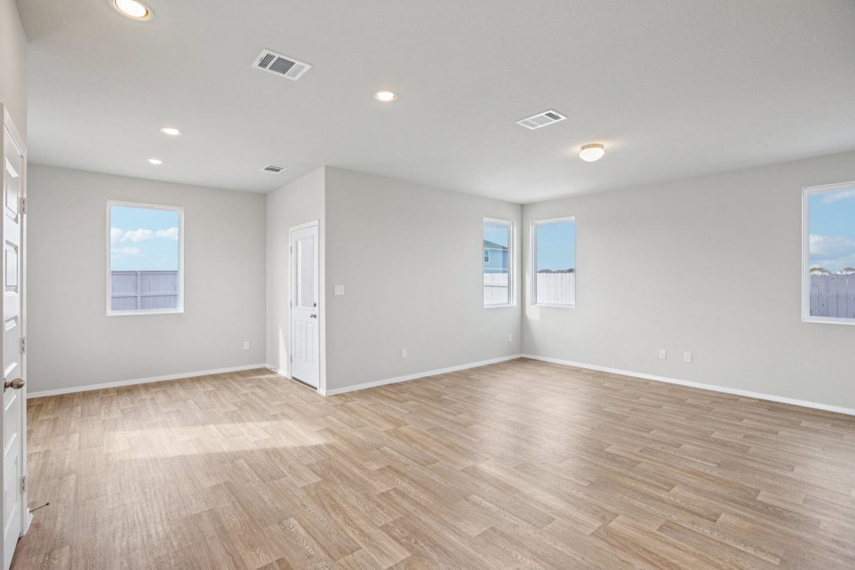 Image of a living room with light grey walls, light brown wood-look flooring, windows and white trim