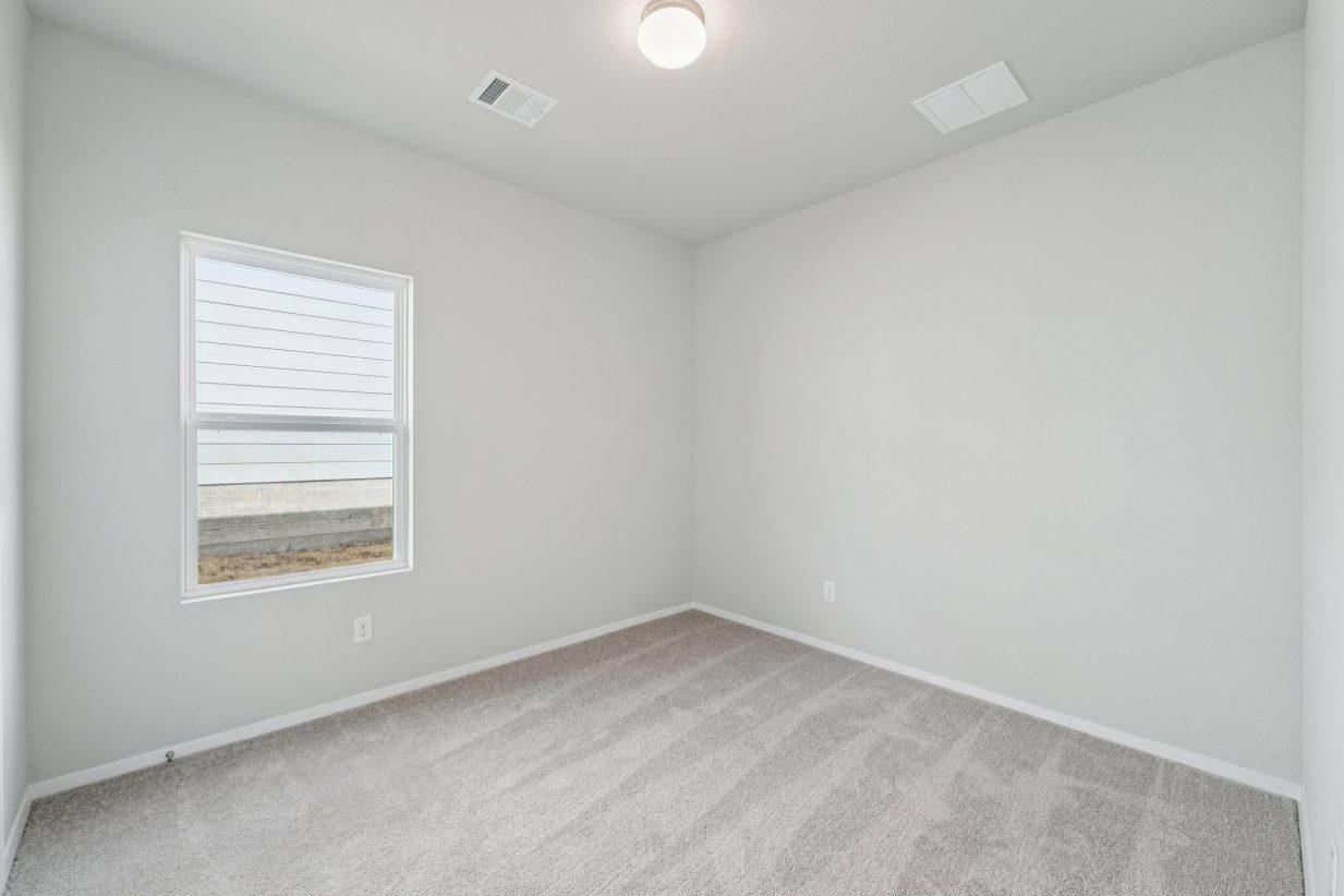 Image of a bedroom with light grey walls, tan carpeting, a window and white trim