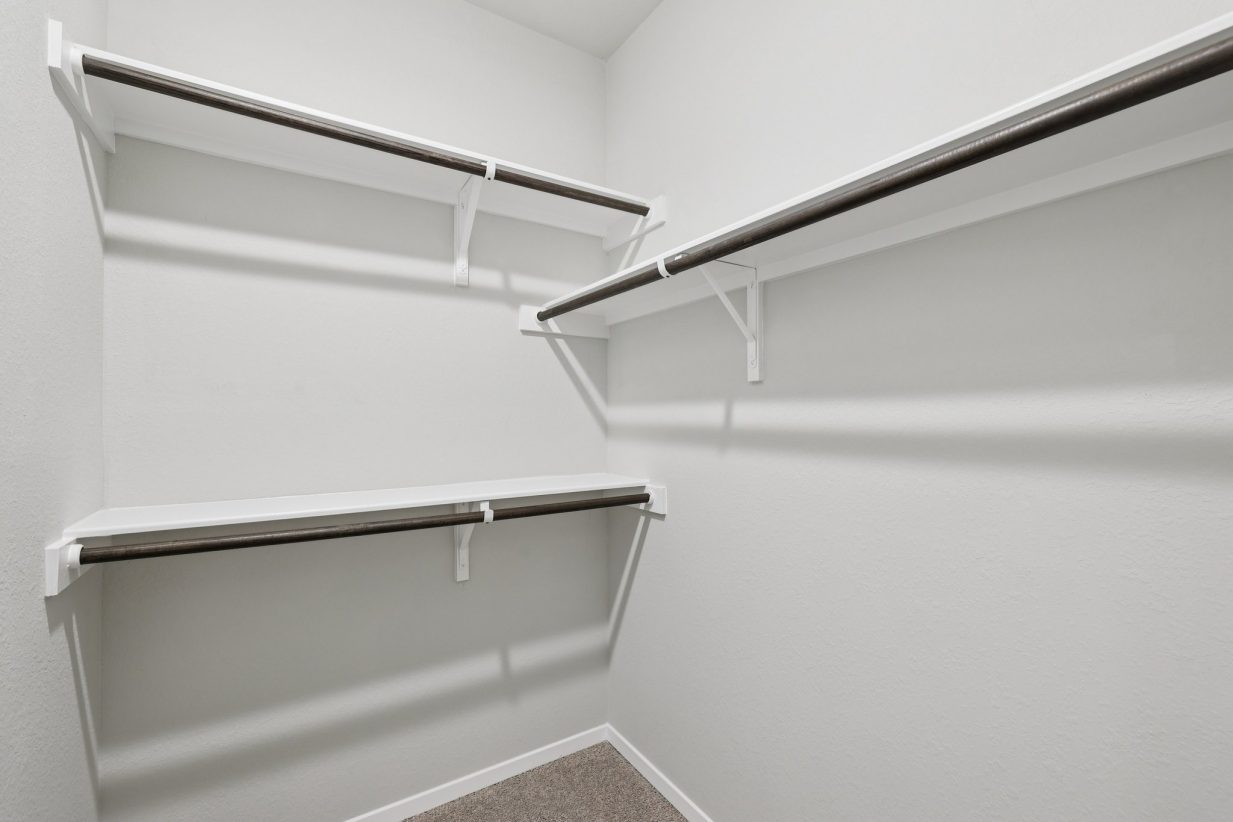 Image of a closet with light grey walls, white shelves and wooden rods