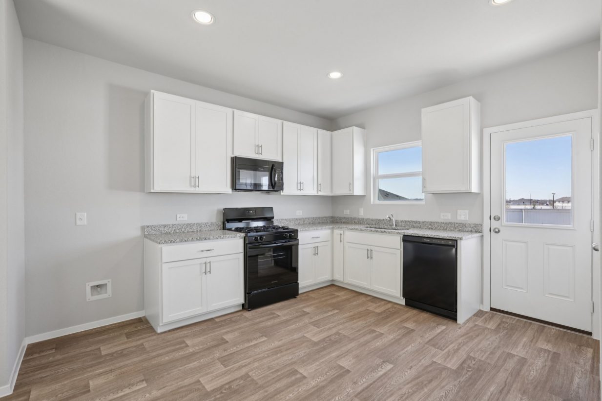 Image of an L-shaped kitchen with white cabinets, granite countertops, black appliances and a window above the sink