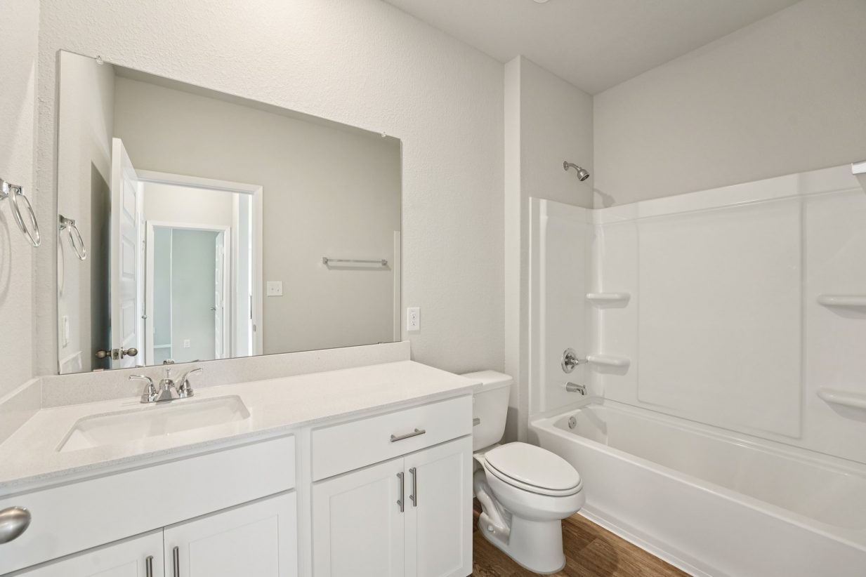 Image of a bathroom with a white dual vanity, white cabinets, a large mirror and a shower and tub