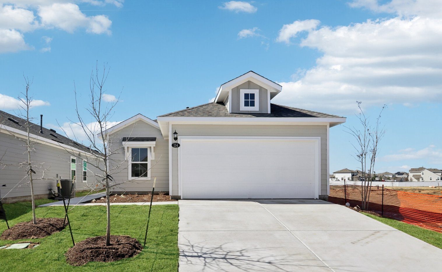 Image of the front exterior of a grey one story house with a white garage door, a cement driveway, a green front yard and a blue sky in the background