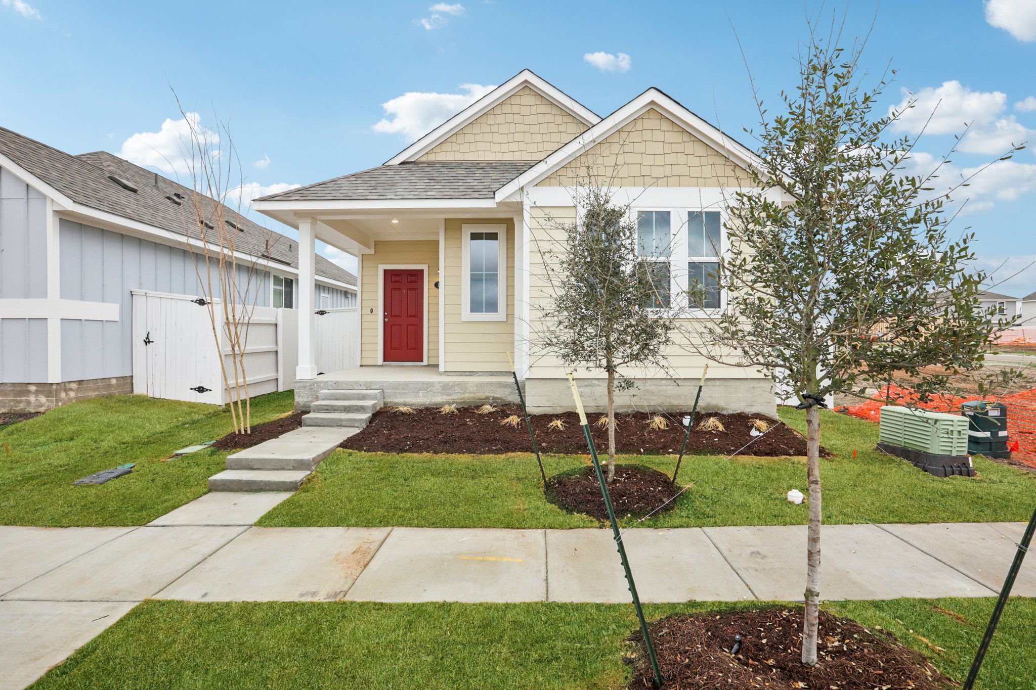 Image of a yellow one story house with a red front door, a green grass front yard, and a blue sky in the baclground