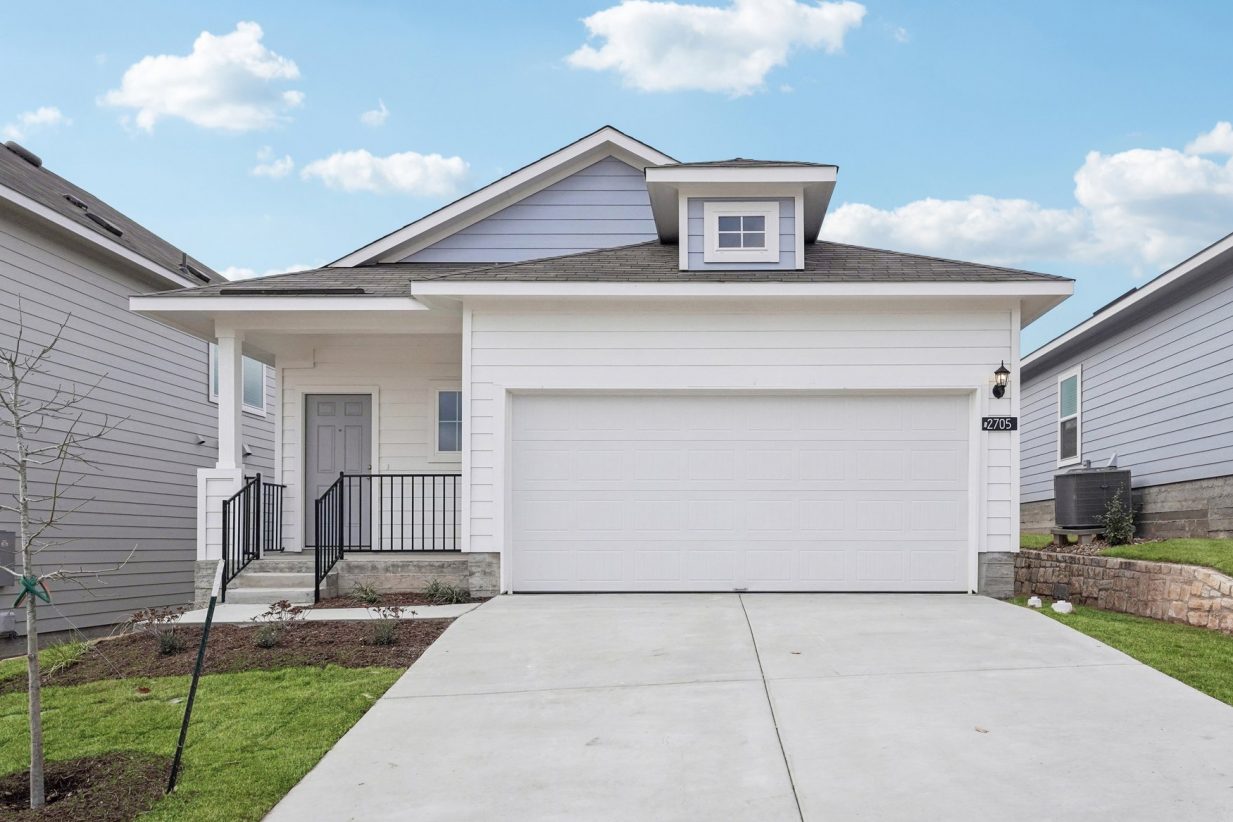 Image of a blue and white one story house with a white garage, a cement driveway, a green grass front yard and a blue sky in the background